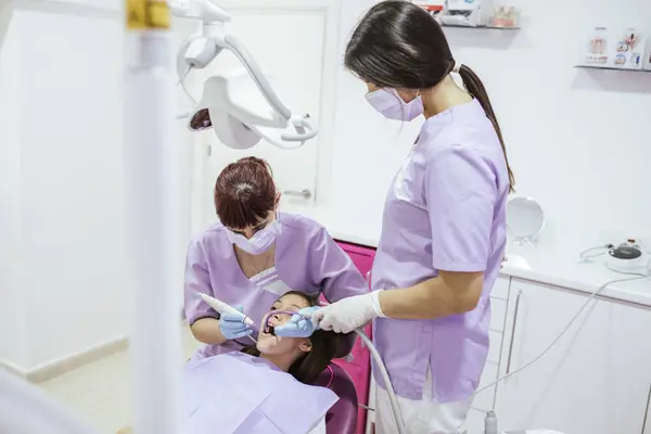 在现代牙科诊所 身穿制服及戴口罩的女牙医 由女性辅助人员治疗病人的牙齿 — 图库照片