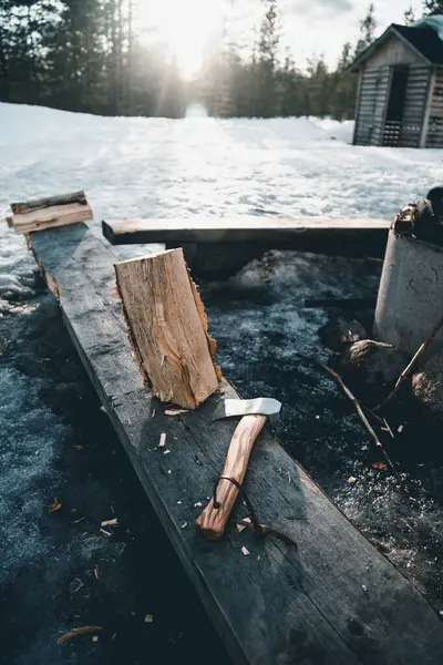 たき火を燃焼し フィンランドの田舎で冬の日に雪の森の中で腰椎の小さなキャビンの近くに置かれた斧でログ — ストック写真