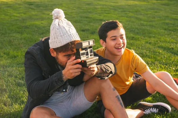 在秋天的公园里 一个年轻的男人带着相机坐在草地上 给一个快乐的妻子和小孩拍照 — 图库照片