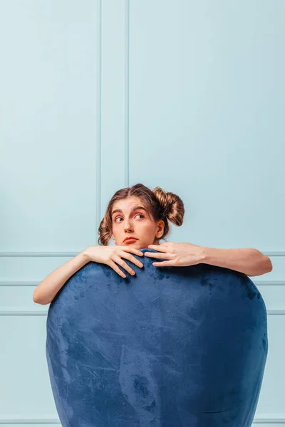 Garota adolescente assustada em uma poltrona azul no fundo azul-turquesa olhando para longe — Fotografia de Stock