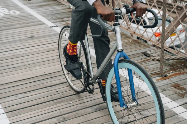 Ausgeschnittenes Bild eines gut gekleideten Geschäftsmannes, der mit dem Fahrrad auf einer Holzstraße zwischen roter Metallkonstruktion in New York fährt — Stockfoto