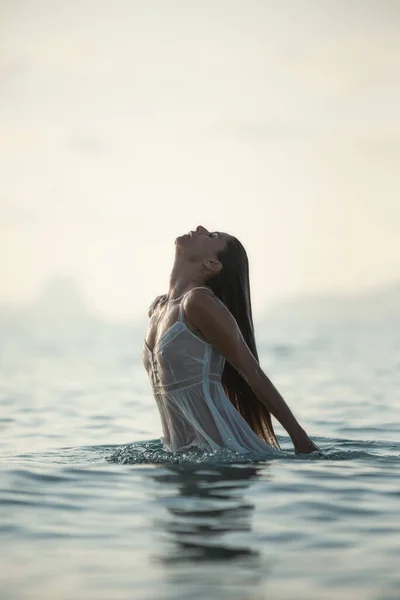 Senhora sexy em vestido úmido translúcido emergindo da água do mar na noite calma na natureza — Fotografia de Stock