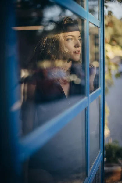 Young smiling woman in black bodysuit looking away pensively and smiling while standing near window at home — Stock Photo