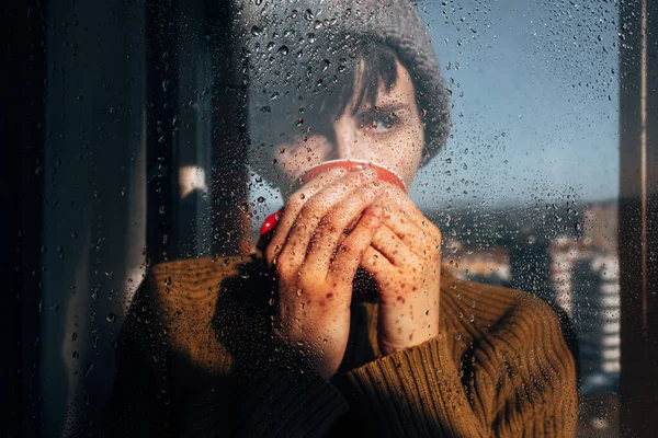 Mujer pensativa bebiendo café cerca de la ventana - foto de stock