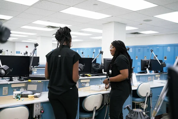 Mulheres afro-americanas com tranças e dreadlocks em pé perto da mesa e falando uns com os outros enquanto trabalham em laboratório juntos — Fotografia de Stock