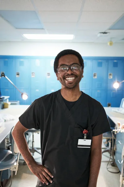 Счастливый афроамериканец с рукой на талии улыбается и смотрит в камеру во время работы в современной лаборатории — стоковое фото
