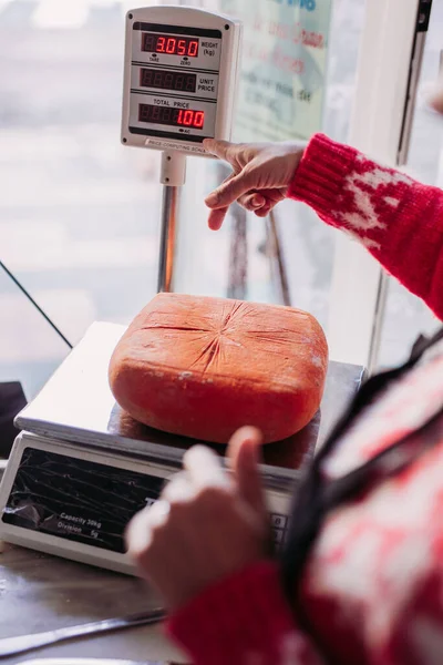 Zugeschnittene unkenntliche Person beim Wiegen von Käse an einer Maschine mit elektronischer Anzeige, die auf der Theke eines örtlichen Feinkostgeschäfts steht — Stockfoto