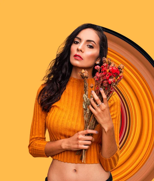 Впевнена молода жінка модель в модному оранжевому городі, тримаючи букет свіжих квітів і дивлячись на камеру, стоячи проти яскраво помаранчевої стіни з геометричним орнаментом в студії — стокове фото