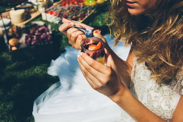 From above view of anonymous young lady in elegant white wedding dress eating delicious sweet strawberry dessert with spoon during outdoor lunch — Stock Photo