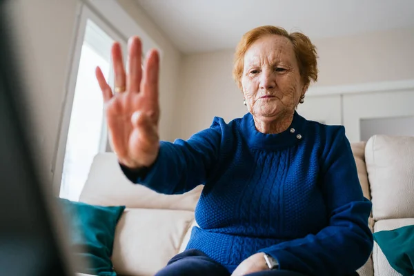 Low angle of smiling aged female gesturing and greeting friend while having video conversation on laptop during self isolation for coronavirus prevention at home — Stock Photo