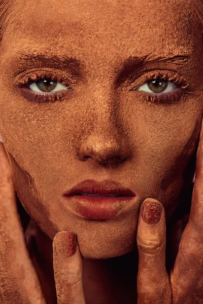 Jeune belle femme avec du chocolat en poudre sur le visage toucher la peau et en regardant la caméra — Photo de stock