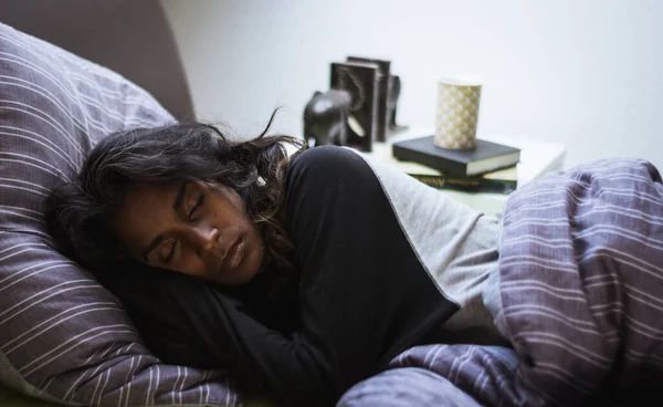 Vista laterale di riposo donna indiana in pigiama party riposando pacificamente su letto accogliente su morbido cuscino e coperta in camera da letto luce — Foto stock