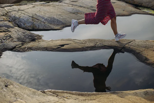 Side view of anonymous crop female traveler in white sneakers and skirt running between puddles on rocky ground on sunny day — Stock Photo