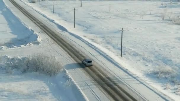 Автомобиль едет по дороге в заснеженном лесу. Вид с воздуха на снежный лес с высокими соснами и дорогу с автомобилем зимой — стоковое видео