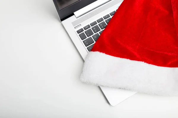 Bilgisayarın beyaz izole bir arka planı var. Dizüstü bilgisayarında bir santaclaus şapkası var. Çalışma yılının sonunda. Tatil satışları.