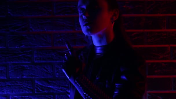 Портрет дівчини в кіберпанк-костюмі в неоновому барвистому світлі. Світловий меч і контактні лінзи . — стокове відео