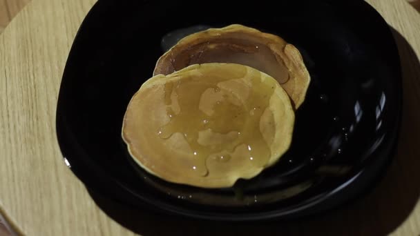 Zwei Pfannkuchen drehen sich auf einem schwarzen Teller. Pfannkuchen mit Honig überzogen. — Stockvideo
