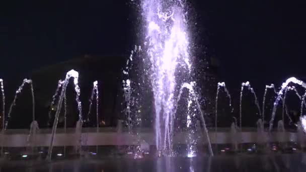 Фонтан в ночном центре города. Медленное видео вода затем поднимается снова она падает. В нижней части фонтана огни сияют разными цветами . — стоковое видео