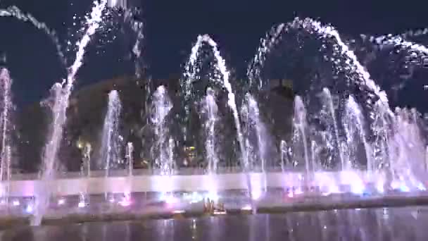Фонтан в нічний час в центрі міста. Потім вода знову піднімається вгору, падає. На дні фонтану світяться вогні різних кольорів . — стокове відео