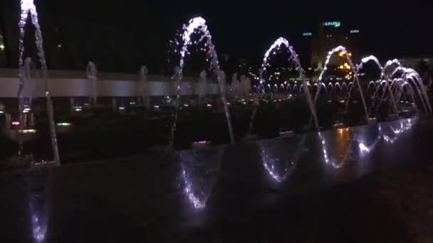 Fuente en el centro nocturno. Lento agua de vídeo a continuación, se eleva de nuevo cae. En la parte inferior de las luces de la fuente brillan en diferentes colores . — Vídeo de stock