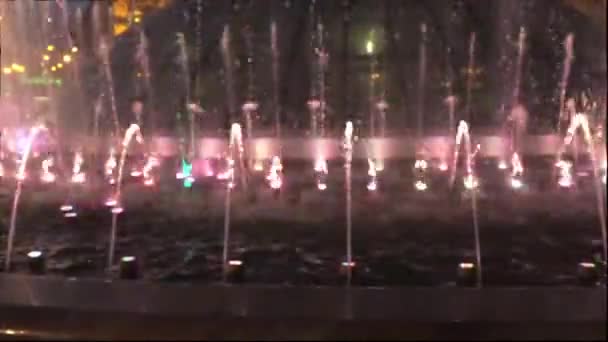 Фонтан в ночном центре города. Вода снова поднимается и падает. В нижней части фонтана огни сияют разными цветами . — стоковое видео