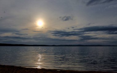 gri bulutların arasından göl üzerinde puslu güneş parlıyor