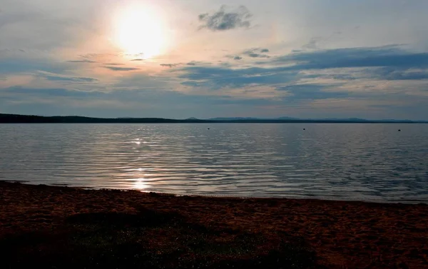 Hazy sun over the lake shines through the gray clouds — Stock Photo, Image