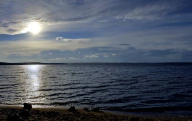 gri bulutların arasından göl üzerinde puslu güneş parlıyor