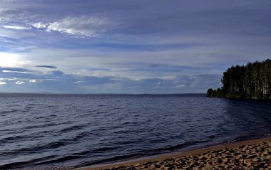 gri bulutların arasından göl üzerinde puslu güneş parlıyor