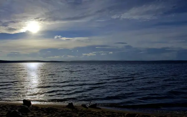 gri bulutların arasından göl üzerinde puslu güneş parlıyor