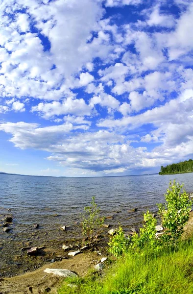 Céu azul brilhante com nuvens brancas sobre a costa do lago — Fotografia de Stock