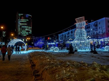 Şehir meydanında gece çelenklerle aydınlatılan yeni yıl kardan adam figürü