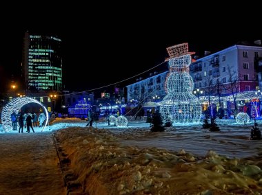 Şehir meydanında gece çelenklerle aydınlatılan yeni yıl kardan adam figürü