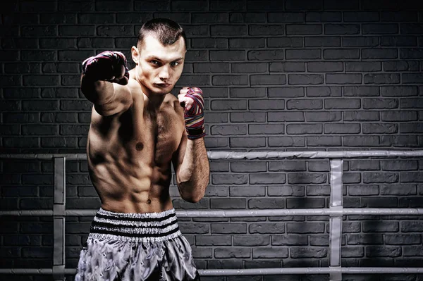 Thai boxer stands in the ring and punches in front of him. The c