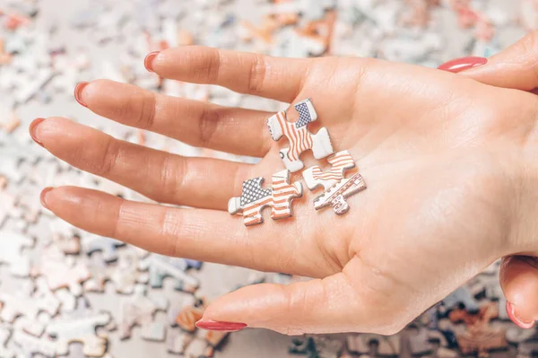 Woman sprawling three puzzles with the US flag on her hand. Economic and political concept. Mixed media