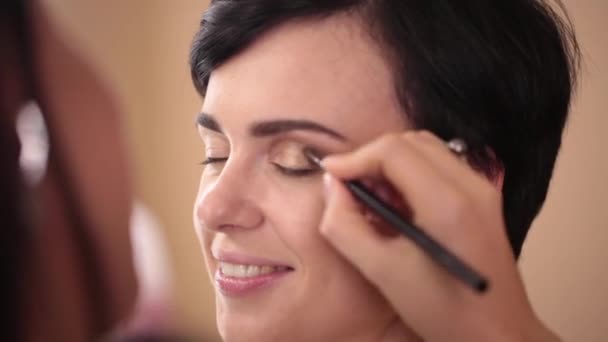 En make-up artist målar en flickas ögonlocket. Närbild. — Stockvideo