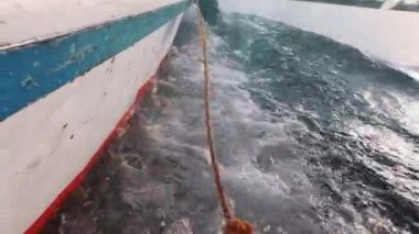 Kayığın yan tarafında kırmızı ve mavi çizgileri olan eski bir tekneden sallanan ip köpüklü dalgalar boyunca sallanıyor. Luxor, Mısır. Yumuşak odak