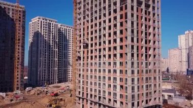 İnşaat alanının görüntüsünde, kamera bina boyunca yükseliyor, şehri ve vinçleri gösteriyor.