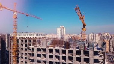 En üst kattaki inşaatçılar, şehrin arka planında vinç olan bir yerdeki resmi çalışmaları kaldırıyorlar.