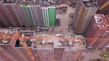 Şehirdeki bir ormanın arka planında vinçleri olan yüksek katlı tuğladan yapılmış bir binanın üst görüntüsü.