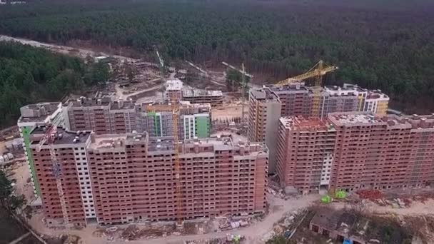 市内の森林を背景に クレーンのあるレンガ造りの高層ビルの建設のトップビュー — ストック動画