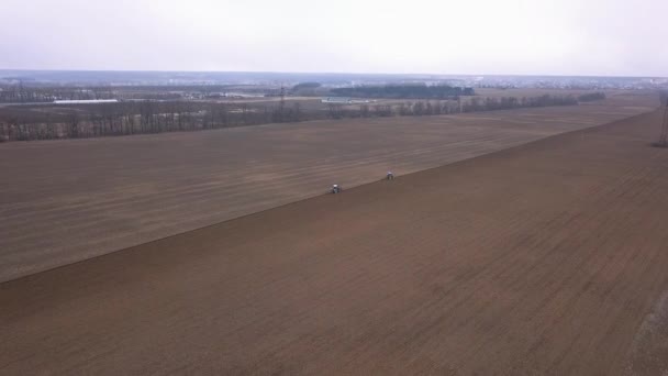 Une approche de deux tracteurs bleus labourant champ, avec une perspective d'ouverture du champ et le village et la route 