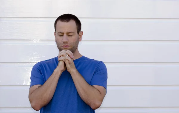 Man praying with white background wearing a blue shirt.