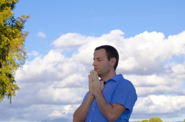 Bulutlar ve ağaçları içinde belgili tanımlık geçmiş ile dua adam.