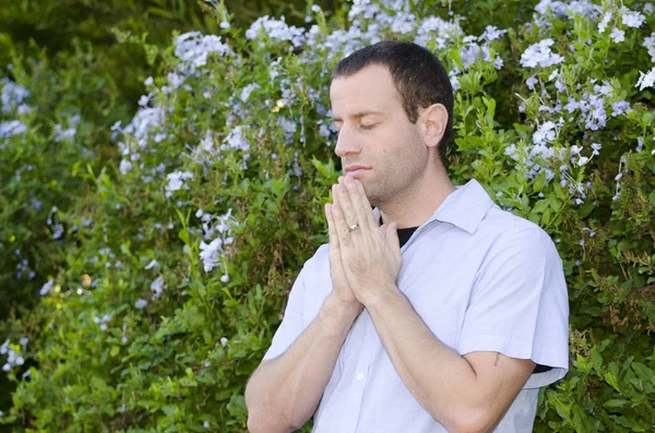 Man praying with hands together and eyes closed.