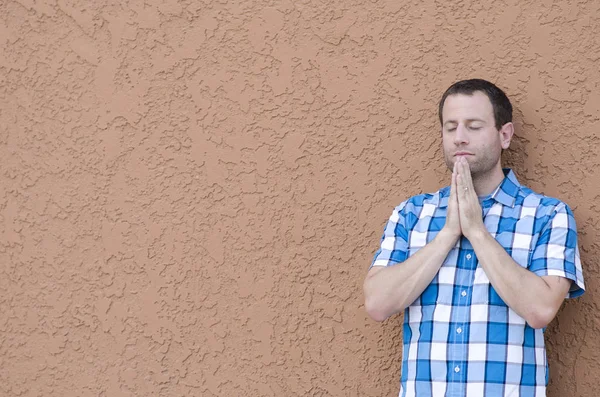 Adam arka plan olarak bir bej sıva duvar ile dua.