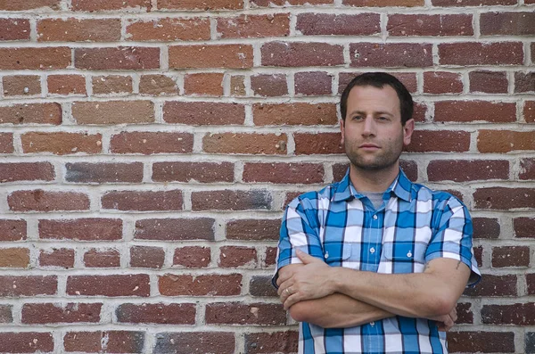 Bir tuğla duvara yaslanmış bir adam portresi.