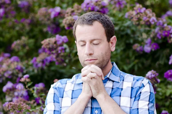Man praying outside in front of purple flowers. — Stock Photo, Image