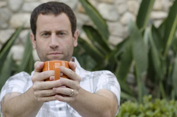 Onun önünde turuncu bir kupa mug odak ile tutan adam. 