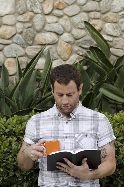 Adam açık havada bir kupa tutarken bir kitap okuma.